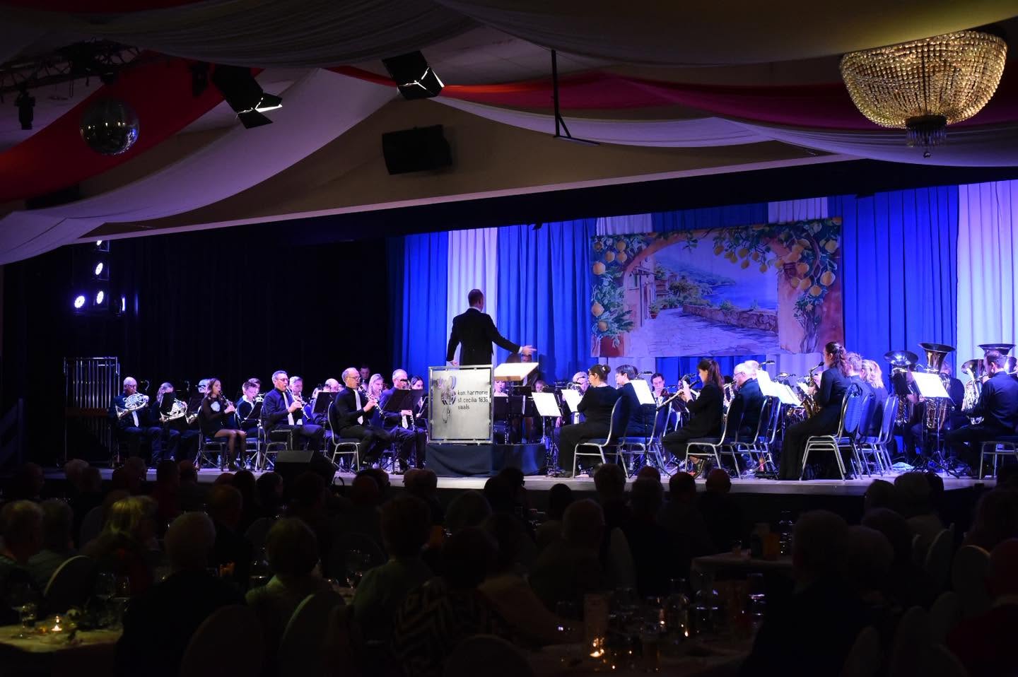 Het harmonieorkest speelt onder leiding van de dirigent voor een mediterraan decor
